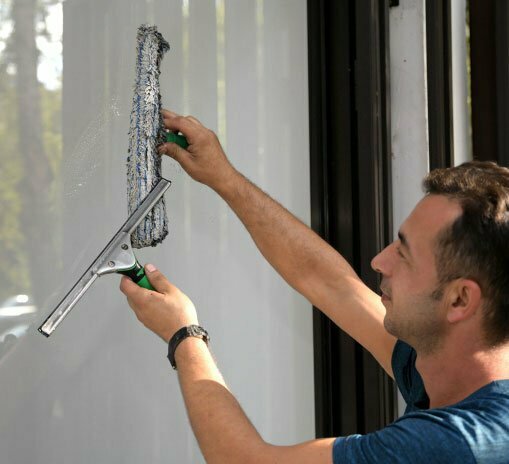 Un homme nettoyant une fenetre a l'aide d'un chamois et d'un squeegee.