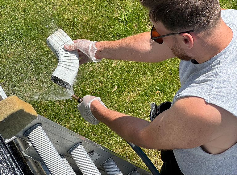 Laveurs nettoyant l'interieur d'un coude d'une gouttieres.